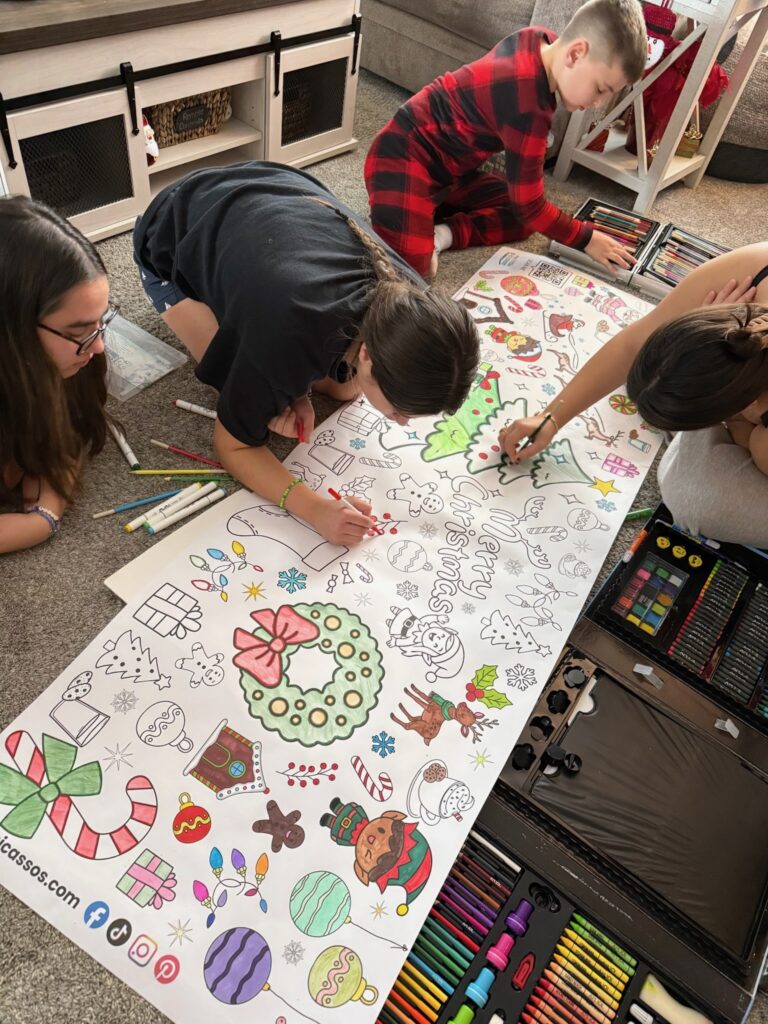 young boy with teenage sisters sitting on the floor coloring a giant christmas banner