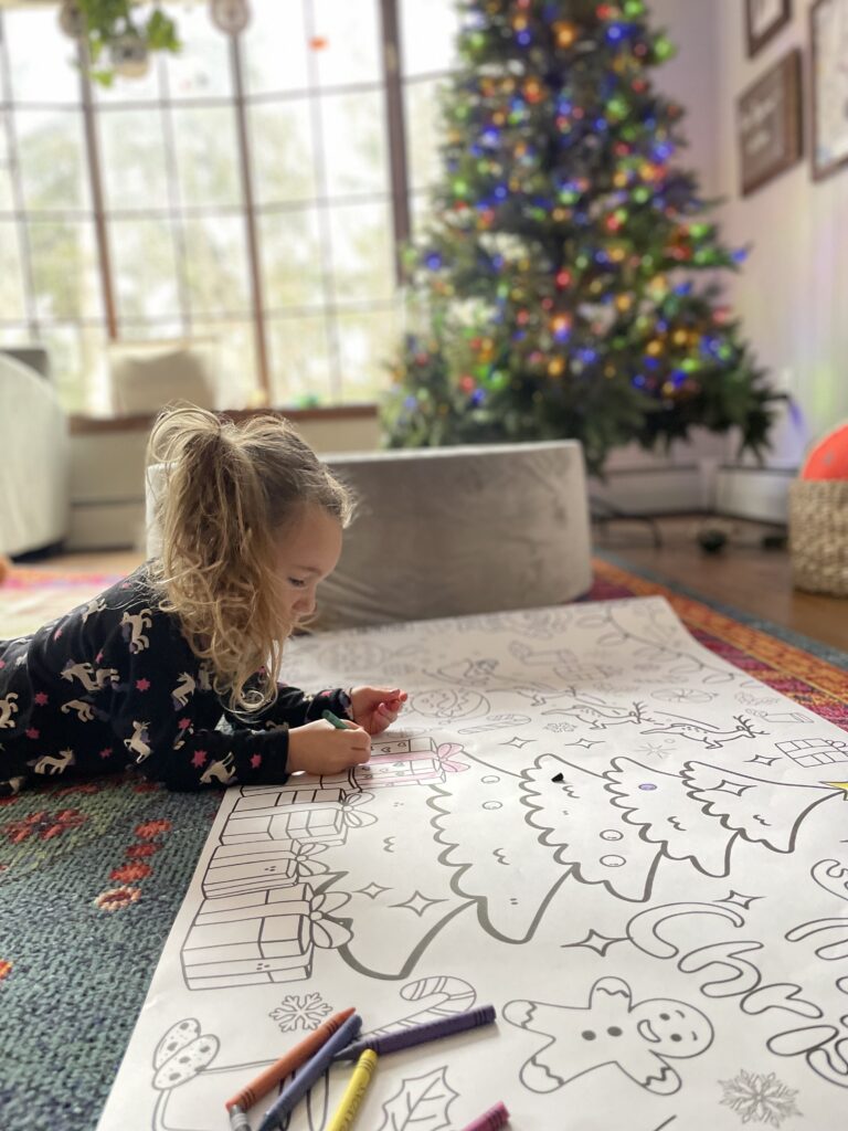 Little girl laying on belly coloring a giant christmas banner